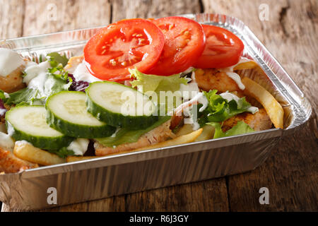 Delicious dinner Dutch kapsalon of french fries, chicken, fresh salad, cheese and sauce close-up in a foil tray on the table. horizontal Stock Photo