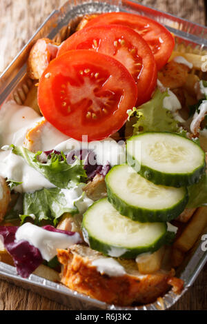 Dutch fast food kapsalon of french fries, chicken, fresh salad and sauce close-up in a foil tray on the table. vertical Stock Photo