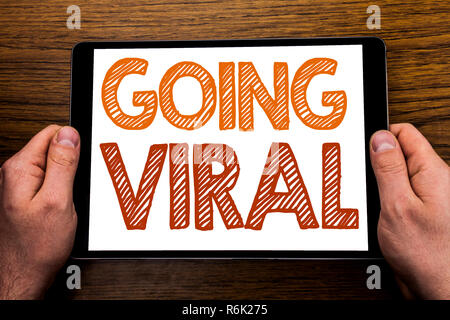Hand writing text caption Going Viral. Business concept for Social Viral Business Written on tablet laptop, wooden background with businessman hand, finger holding PC. Stock Photo