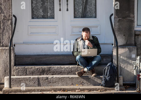 MONTREAL, CANADA - NOVEMBER 4, 2018: Young Caucasian Male, digital nomad, sitting and using his laptop, Apple Macbook, to get wifi internet connection Stock Photo