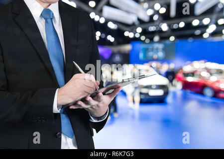 Double exposure of saleman hands holding trade booking with blurred background of new car displayed in showroom dealer, buying new car. Stock Photo