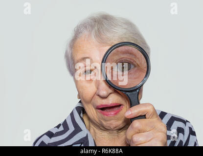 portrait of senior woman looking through a magnifying glass over white background Stock Photo