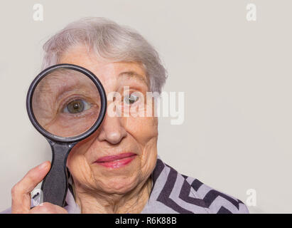 portrait of senior woman looking through a magnifying glass over white background Stock Photo