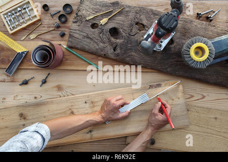 hands carpenter work the wood, measuring with meter and pencil old rustic wooden boards, top view with tools on background Stock Photo