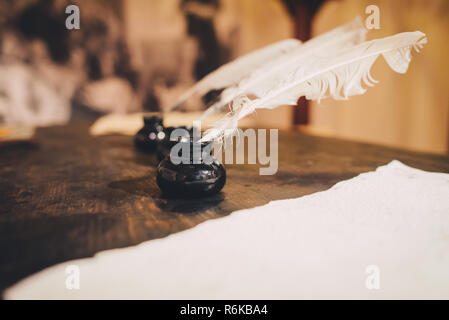 Quill pen with ink and old paper sheet on wooden table; Close-up view; Vintage photo Stock Photo