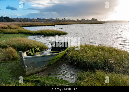 Landscape photograph of the foreshore of a wetland habitat with an old derelict algae covered wooden boat in foreground. Stock Photo