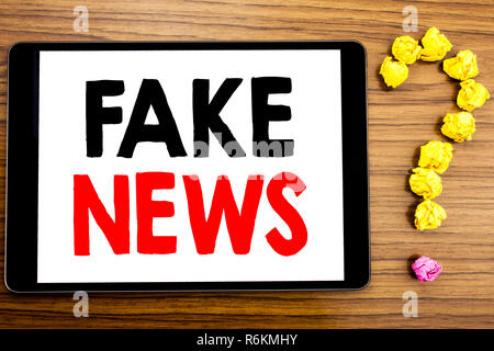 Writing text showing Fake News. Business concept for Hoax Journalism written on tablet computer on the wooden background with question mark made of folded paper. Stock Photo