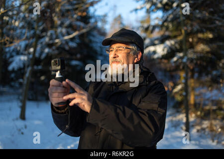 Handsome senior man shotting video with his adventura outdoor camera on a grip handle outdoors on a lovely winter day, enjoying retirement Stock Photo