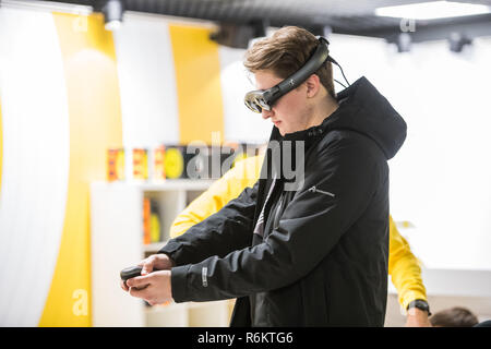 MOSCOW, RUSSIA - OCTOBER 27 2018. Young man using virtual reality headset and drawing with special joystick at technology exhibition. Augmented reality and entertainment concept Stock Photo