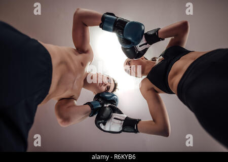 Low angle view of man and woman at kick boxing fighting position. Male and female kick boxers standing against each other with boxing gloves in ring. Stock Photo