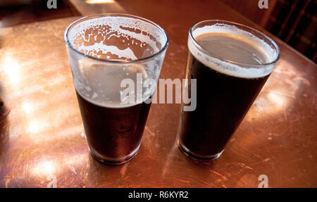 2 tall glasses of dark beer on a copper top table Stock Photo