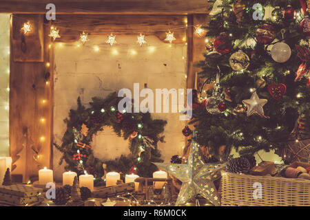 Beautiful Christmas setting, decorated fireplace with wooden mantelpiece fire surround, lit up Christmas tree with baubles ornaments, stars, lights, c Stock Photo