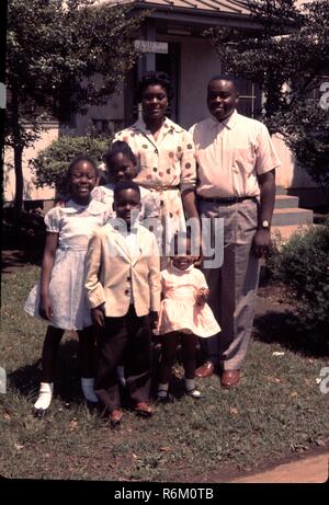 Portrait of African American family standing in front of their home wearing church clothing man in formal shirt and pants woman wearing dotted dress young boy in loafers and formal shirt and three