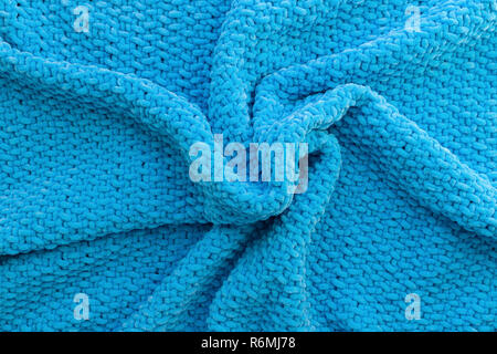 Bright blue knitted plaid made of plush yarn. Soft material. Woolen texture. Handmade craft. Hobby theme. Image for background. Stock Photo