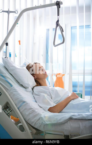 Pretty, young, female patient in a modern hospital room. Getting better fast after a surgery - pensive yet positive, thinking ahead, making plans (shallow DOF  color toned image) Stock Photo