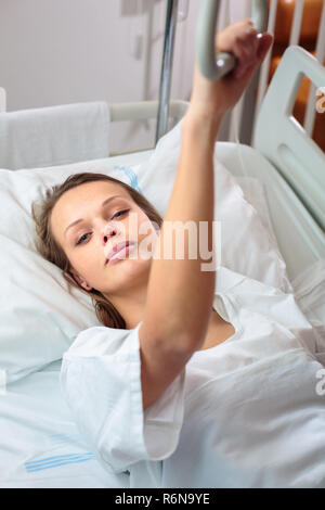 Pretty, young, female patient in a modern hospital room. Getting better fast after a surgery - pensive yet positive, thinking ahead, making plans (shallow DOF  color toned image) Stock Photo