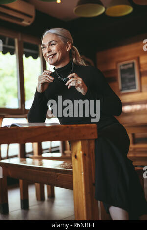 Portrait of smiling mature woman sitting at coffee shop and looking away. Senior female at cafe looking away and smiling. Stock Photo