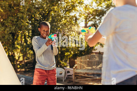 Two kids playing with water guns in backyard. Children enjoys playing with squirt guns outdoors. Stock Photo
