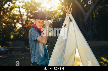 Portrait of young boy posing in cowboy hat by a backyard garden teepee. Little boy having fun in the backyard outdoors. Stock Photo