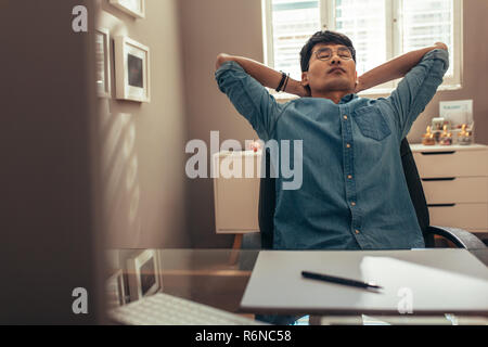 businessman relaxing on chair leaning backwards with hands behind his head. Designer taking break from work for mind relief. Stock Photo