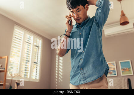 Low angle view of asian man talking on mobile phone with hands in head. Man looking stressed while talking on cell phone at home. Stock Photo