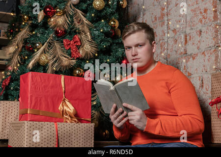Handsome guy is reading a book sitting under the tree surrounded by gifts Stock Photo