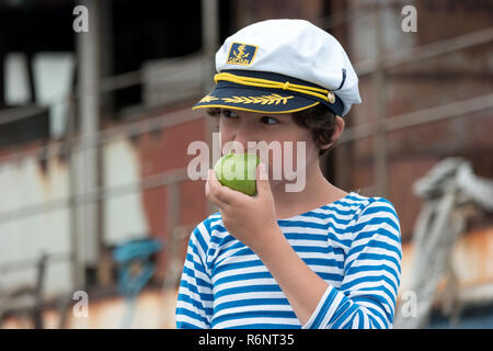 Portrait of a boy in a vest (Telnyashka) and captain's cap. In his hand a green apple. Stock Photo