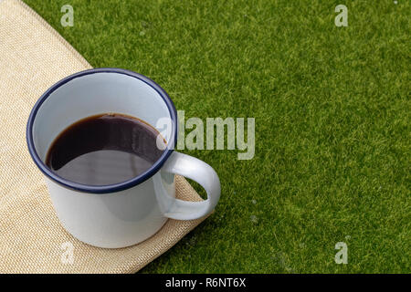 Coffee in white tin cup on grass background. Stock Photo