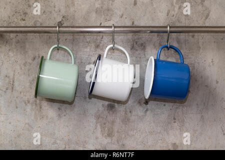 Tin cups hanging on stainless rail on cement wall background. Stock Photo