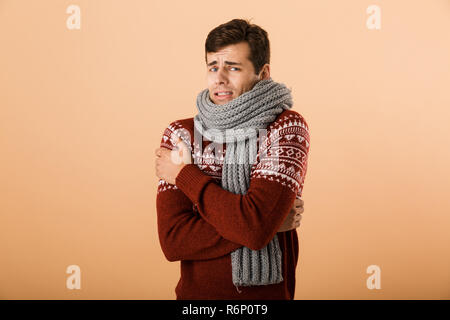 Portrait a young man dressed in sweater and scarf isolated over beige background, shaking Stock Photo