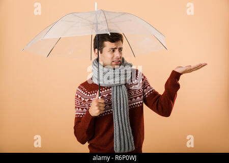 Portrait a sad young man dressed in sweater and scarf isolated over beige background