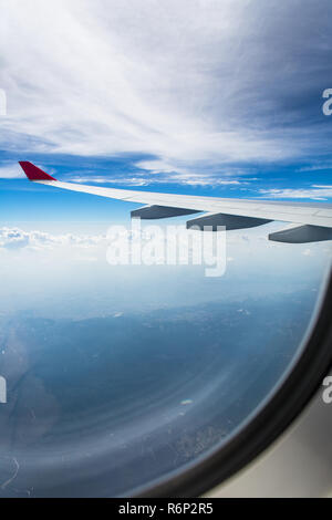 An airplane wing through airplane window with blue sky background Stock Photo