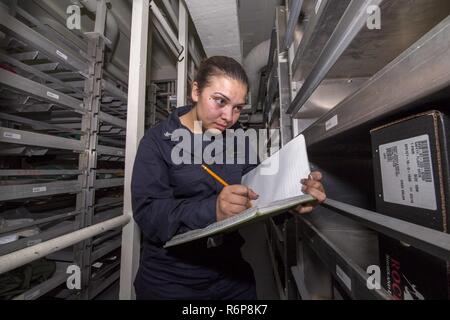 SOUTH CHINA SEA (Aug. 19, 2017) Logistics Specialist 3rd Class Julia Manuma, a native of Waianae, Hawaii, assigned to the amphibious assault ship USS America (LHA 6) Supply department, conducts inventory of flight clothing in the ship’s flight clothing store. America, part of the America Amphibious Ready Group, with embarked 15th Marine Expeditionary Unit, is operating in the Indo-Asia Pacific region to strengthen partnerships and serve as a ready-response force for any type of contingency. Stock Photo