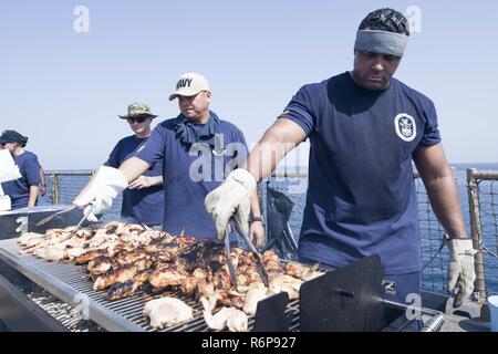 U.S. 5TH FLEET AREA OF OPERATIONS (Sept. 16, 2017) Senior Chief Engineman Daniel Lieurance (right), a native of Temecula, California, and Master Chief Jose Valdes, a native of San Diego, both assigned to the engineering department aboard the amphibious dock landing ship USS Pearl Harbor (LSD 52), grill chicken on the ship’s flight deck during a steel beach picnic hosted by the chiefs mess and the Morale, Welfare and Recreation (MWR) committee. Pearl Harbor is part of the America Amphibious Ready Group (ARG) and, with the embarked 15th Marine Expeditionary Unit (MEU), is deployed in support of  Stock Photo