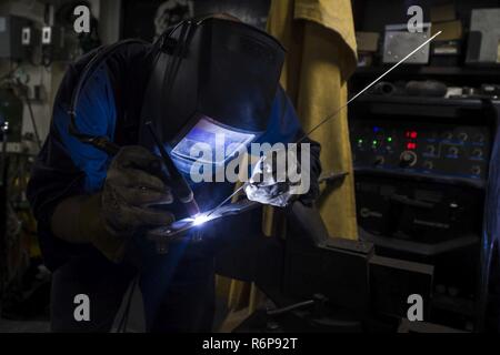 U.S. 5TH FLEET AREA OF OPERATIONS (Sept. 20, 2017) Hull Technician 3rd Class Joseph Fleming, a native of Merced, California, assigned to the engineering department aboard the amphibious dock landing ship USS Pearl Harbor (LSD 52), welds studs to a connecting rod for a quick acting watertight door in the ship’s hull technician shop. Pearl Harbor is part of the America Amphibious Ready Group (ARG) and, with the embarked 15th Marine Expeditionary Unit (MEU), is deployed in support of maritime security operations and theater security cooperation efforts in the U.S. 5th Fleet area of operations. Stock Photo