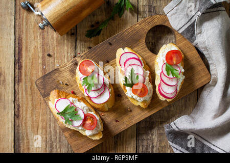 Antipasti snacks for Wine. Brushetta or Crostini with Toasted Baguette,  Cheese, Radish and Tomatoes on a wooden table. Top view flat lay background. Stock Photo
