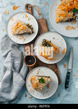 Greek pie spanakopita on gray background. Ideas and recipes for vegetarian or vegan Spanakopita Spinach Pie from fillo pastry. Slices pie on plates. Copy space. Top view or flat lay. Vertical. Stock Photo