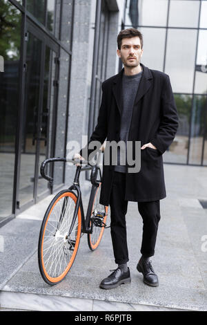 Image of handsome young business man walking outdoors with bicycle. Stock Photo