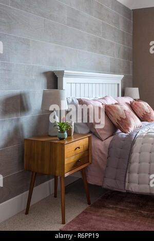Wooden bedaside cabinet with coral pillows on double bed in Hampshire Mill house redesigned by Emma Painter Stock Photo