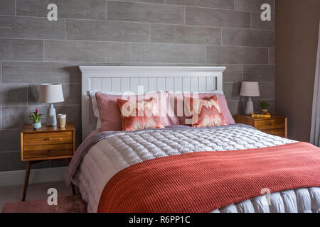 Wooden bedaside cabinet with coral pillows and blanket on double bed in  Hampshire Mill house redesigned by Emma Painter Stock Photo