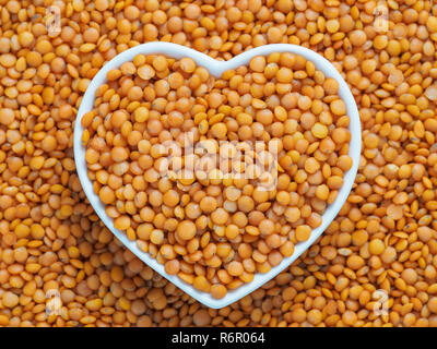 Red orange lentil Football in heart bowl on lentils background Stock Photo