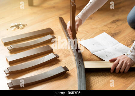 Assembly of wooden furniture, a woman putting together the wooden parts of the dining chair, using instruction. and a furniture screw and allen key. Stock Photo