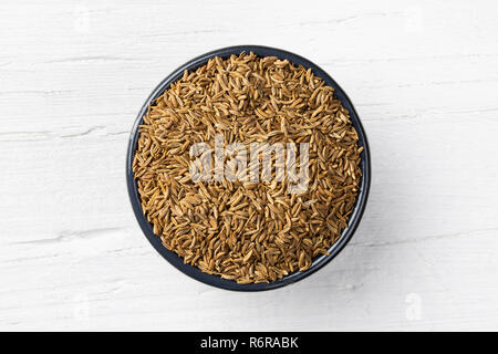 Caraway seeds in round bowl on white wooden background, view directly from above. Stock Photo