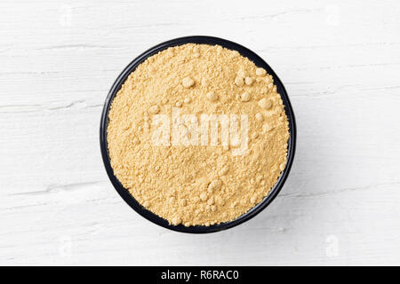Ginger powder in round cast iron bowl on white wooden background, view directly from above Stock Photo