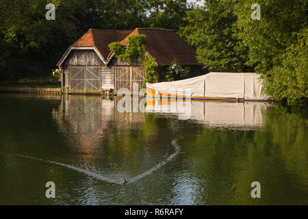 An old boathouse and classic mahogany launch under a canvas cover on the Thames at Mill End, Buckinghamshire Stock Photo