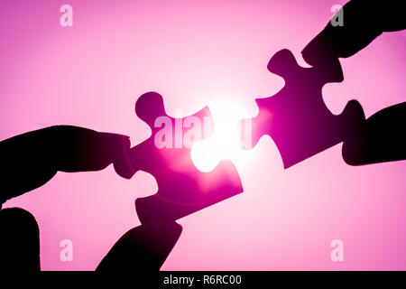 Silhouette of closeup woman's hand connecting a piece of jigsaw puzzle over sunlight effect. symbol of association and connection concept. business strategy. Stock Photo