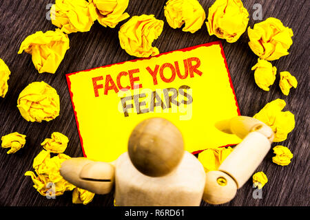 Writing text showing  Face Your Fears. Business photo showcasing Challenge Fear Fourage Confidence Brave Bravery written on Sticky Note Holding By Sculpture on the wooden background Stock Photo