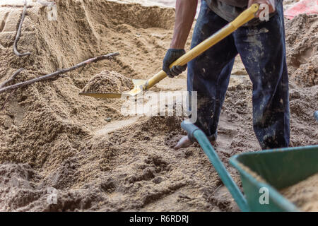 A worker use the shovel to fill the sand into the wheelborrow for construction of new house. Construction tools. Stock Photo