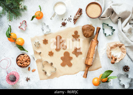 Preparation of gingerbread cookies. Unbaked gingerbread cookies and cookie dough on parchment paper with Christmas decorations around. Top view, flat  Stock Photo
