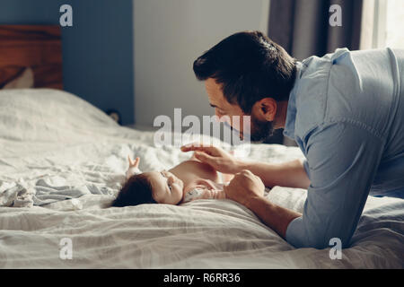 Portrait of middle age Caucasian father talking to newborn baby son daughter. Male man parent smiling to child on bed in bedroom at home. Authentic li Stock Photo